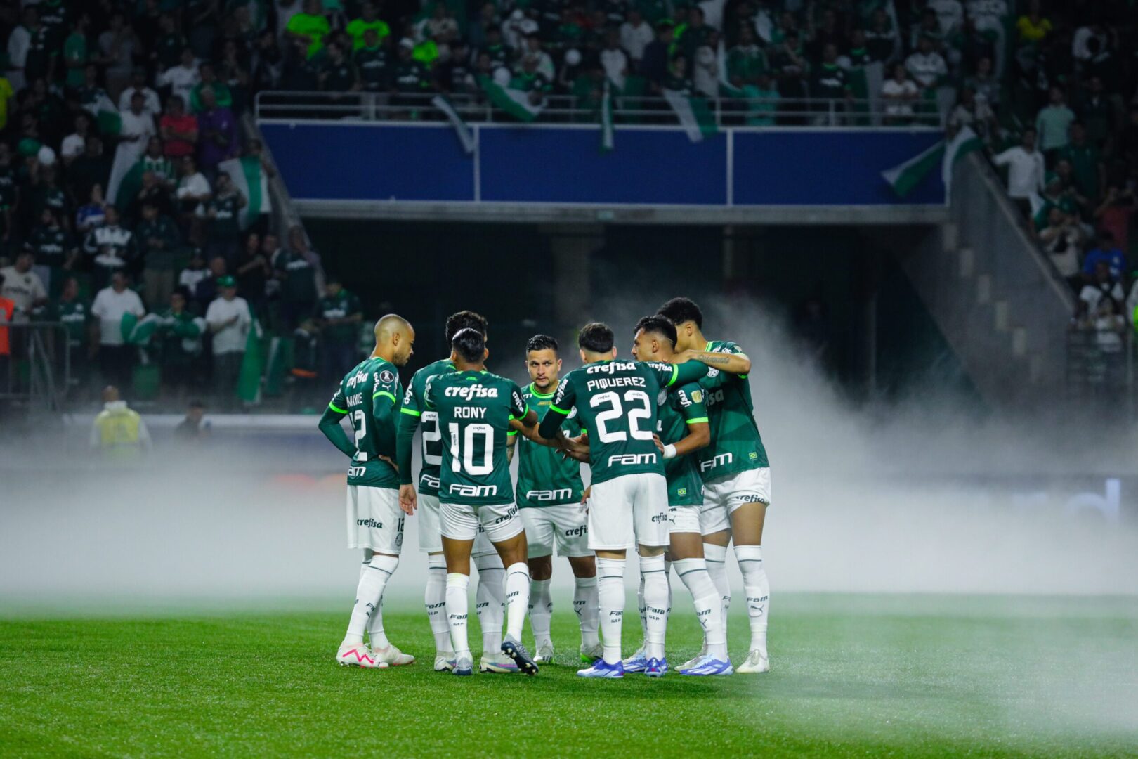 Jogadores do Palmeiras reunidos no gramado com fumaça ao fundo